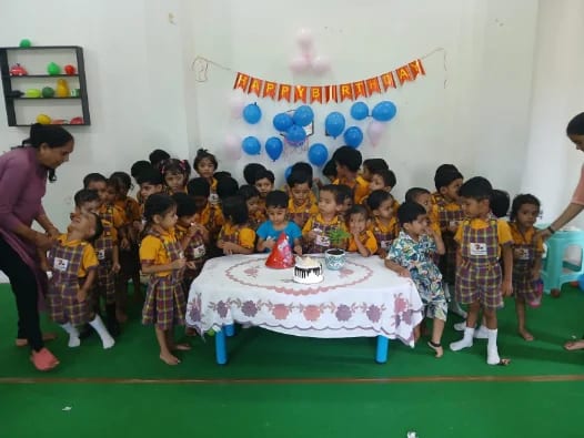 Children gathered around a birthday cake with balloons and a banner behind them
