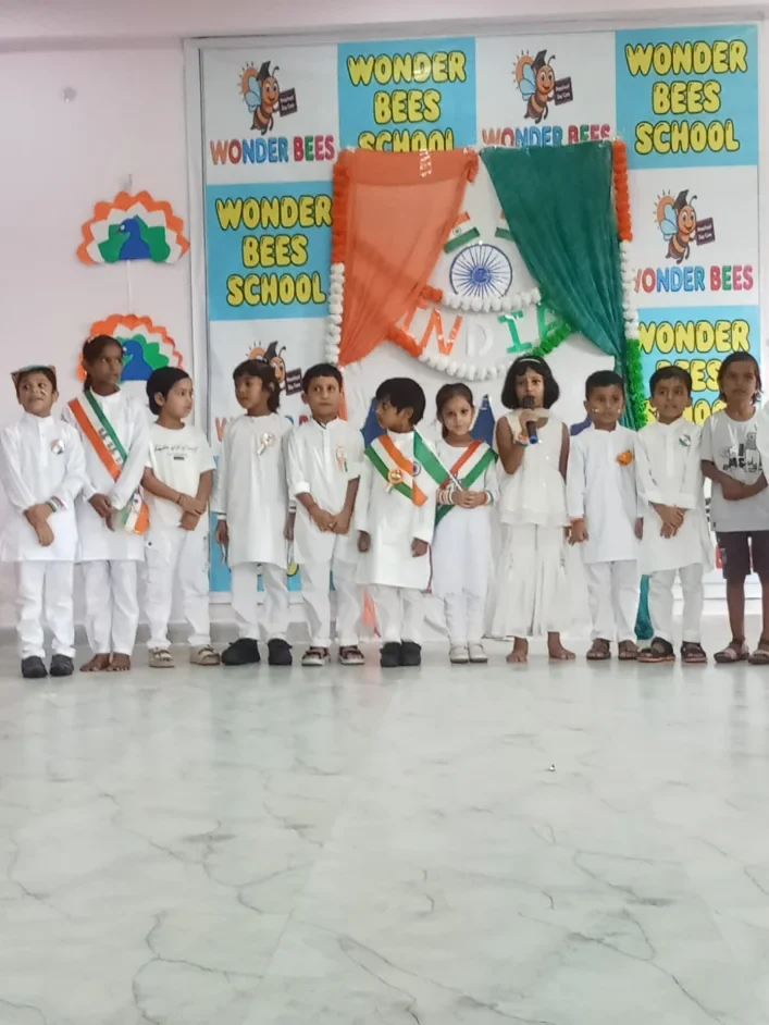 Wonder Bees children in white standing before a school assembly backdrop during an Independence Day program