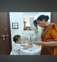 A teacher helping a young child wash their hands at the classroom basin