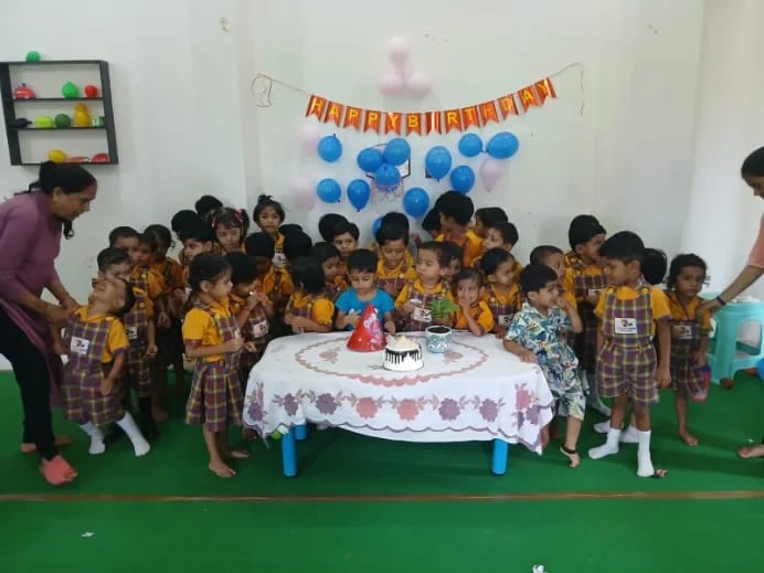 Children gathered around a birthday cake with balloons and a banner