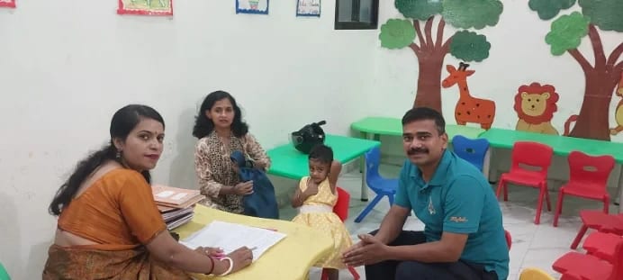 A Wonder Bees teacher at her desk with a child and parents, beside a classroom wall painted with trees and animals