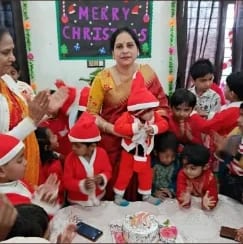 Children and staff in red and Santa hats around a table beneath a hand-made 'Merry Christmas' banner